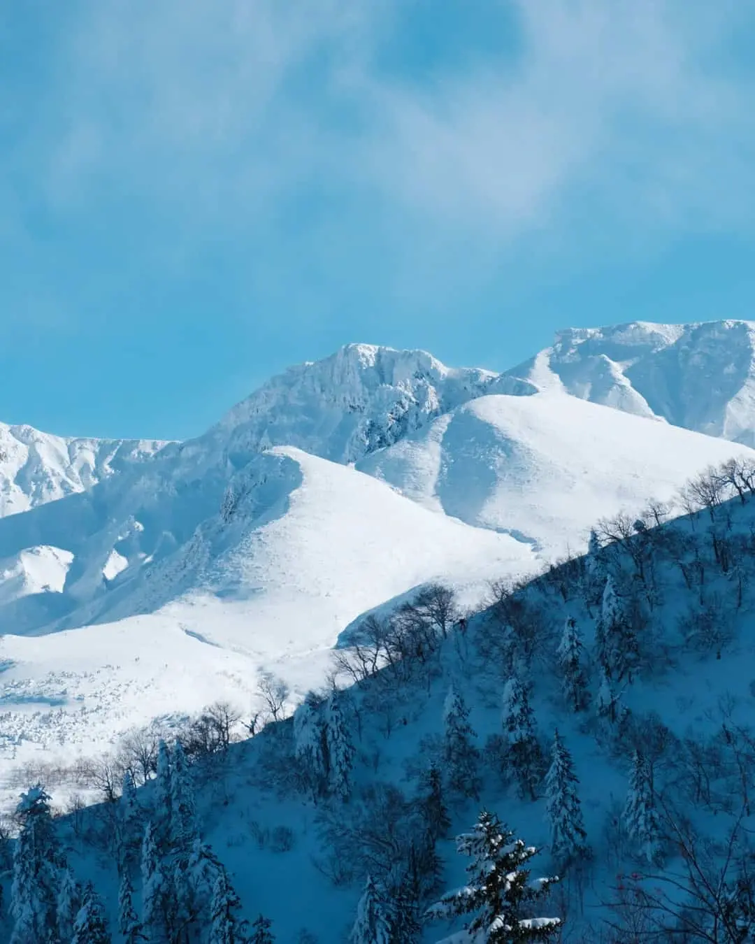 Snow-covered Tokachi mountain range under a blue sky